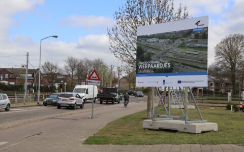 Aankondigingsbord Spoorwegonderdoorgang Vierpaardjes geplaatst bij de huidige spoorwegovergang. Op de foto staan een luchtfoto van het gebied en de logo's van de samenwerkingspartners.