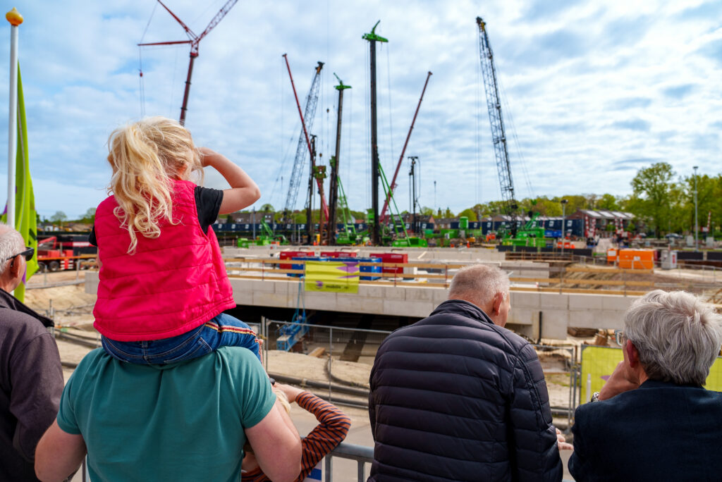 Vader met dochter op de schouders kijken samen naar de werkzaamheden vanaf de kijkerstribune.